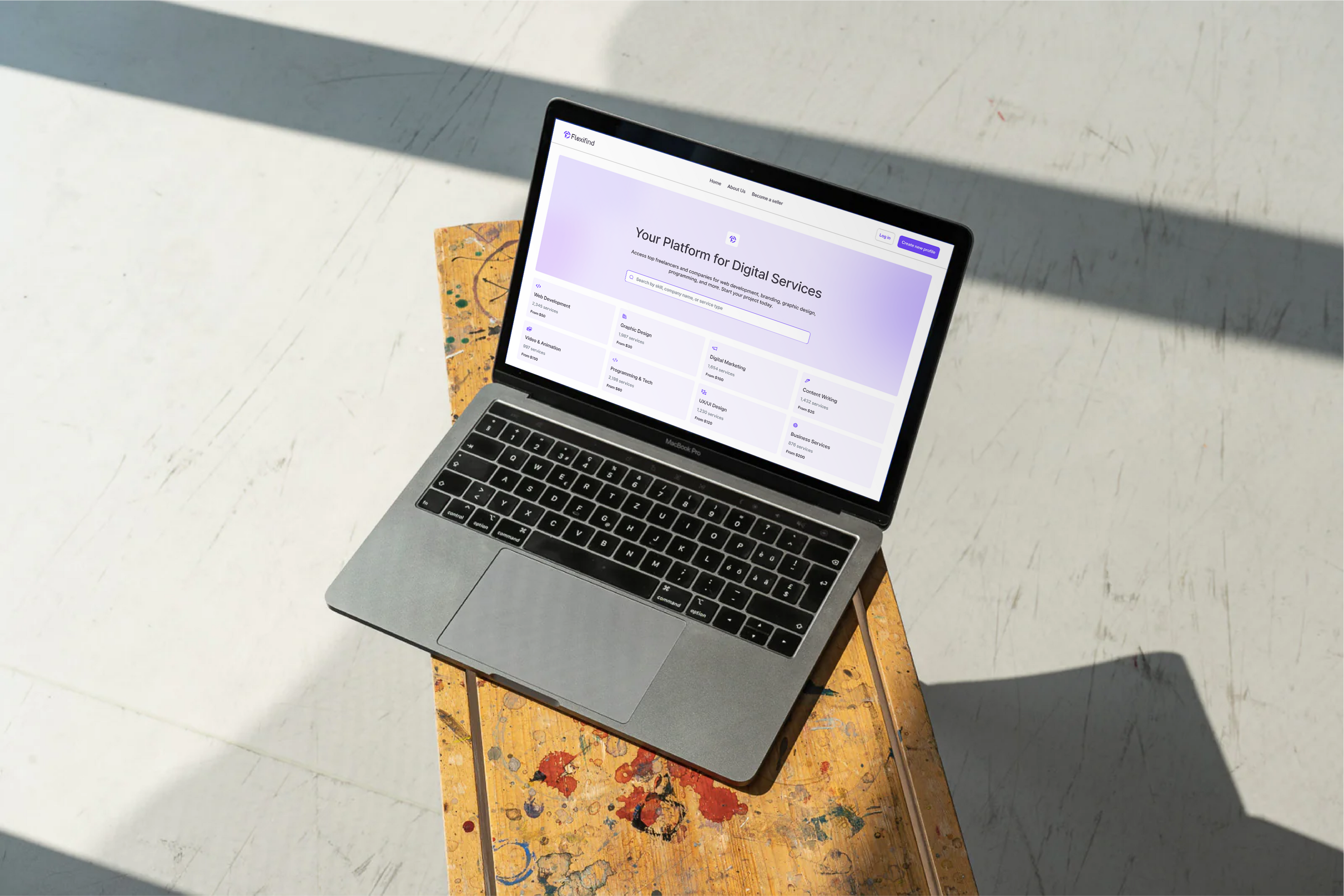 A MacBook on a sunlit patterned surface displaying the Flexifind digital-services marketplace.
